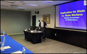 Person in a suit behind a desk giving a presentation.